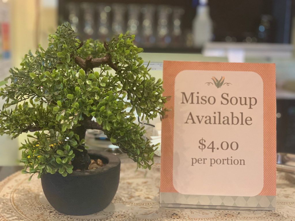 A small bonsai tree is sitting next to a sign that says miso soup available.