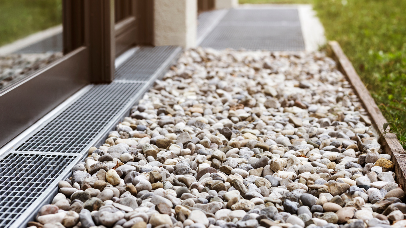 A sidewalk filled with gravel and a metal grate.