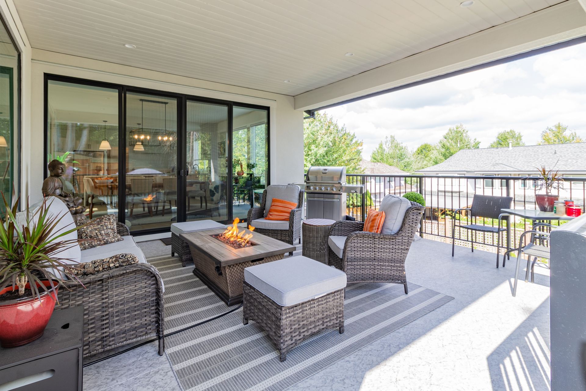 Covered patio with wicker seating, fire pit, and gray outdoor rug overlooking a backyard and pool.