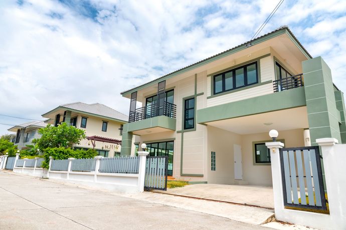 Modern two-story house with green accents and gated driveway on a sunny residential street