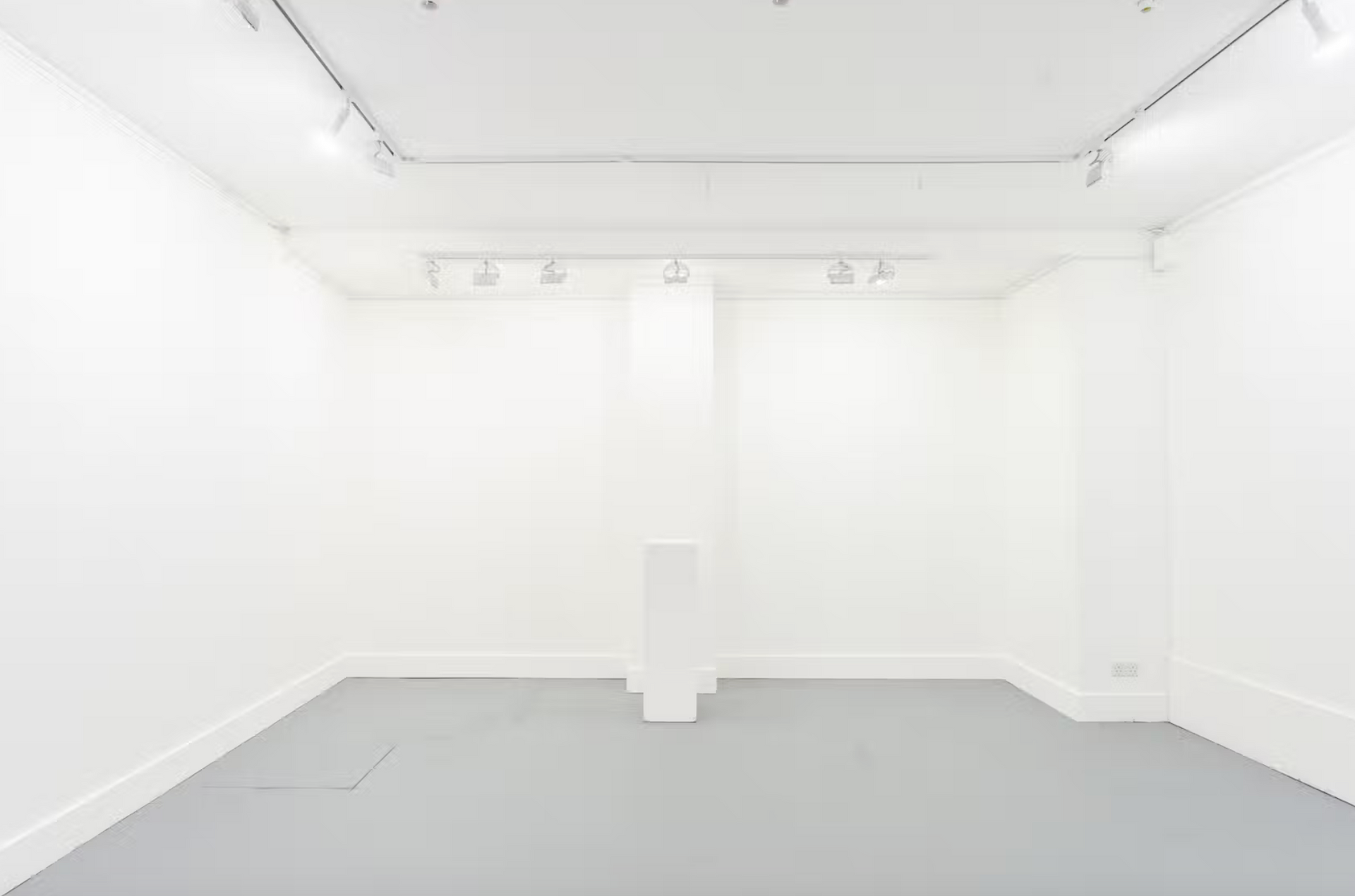 An empty room with white walls and a gray floor.
