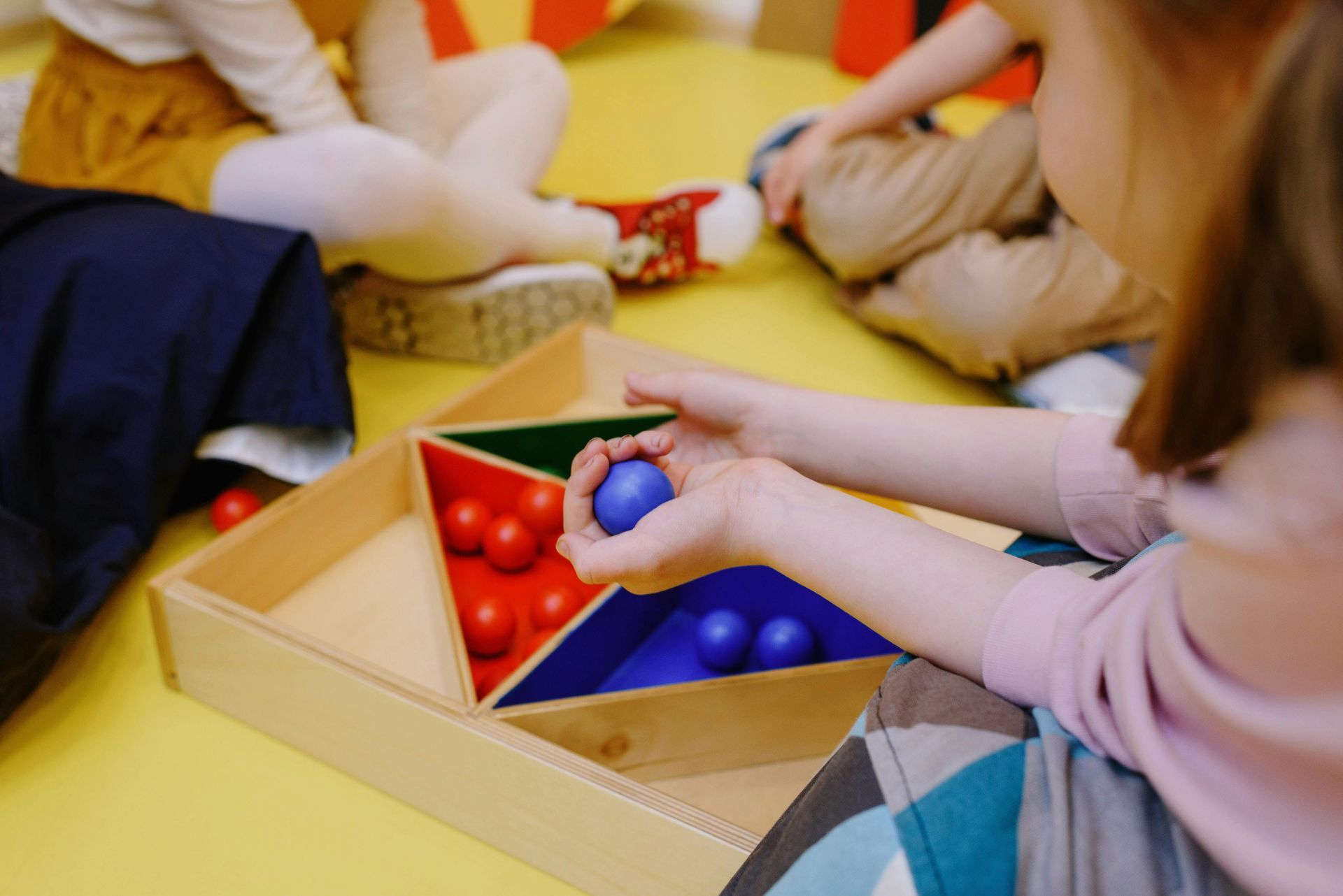 Children sorting red and blue balls into a wooden tray during a classroom activity