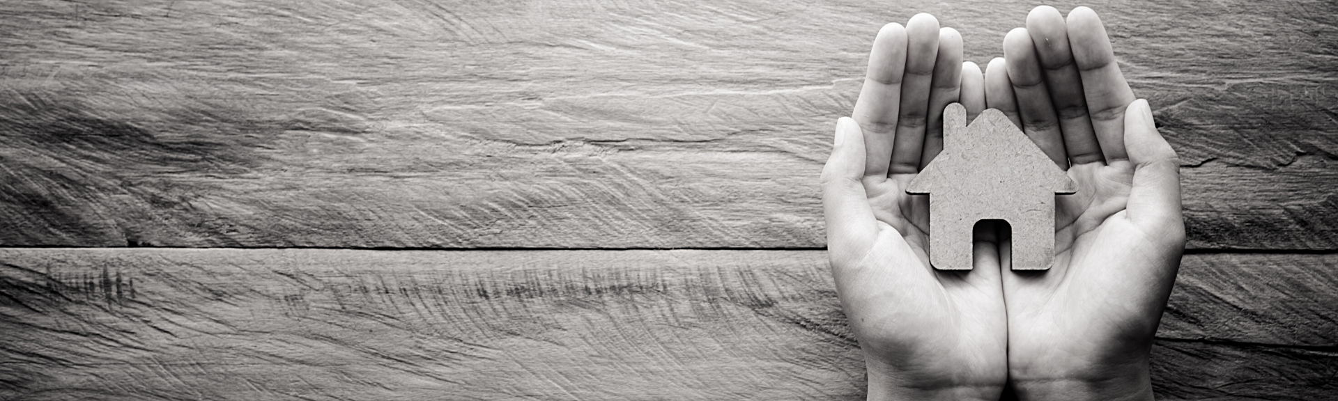 Hands cupping a small house icon on a wooden surface, symbolizing shelter or home protection