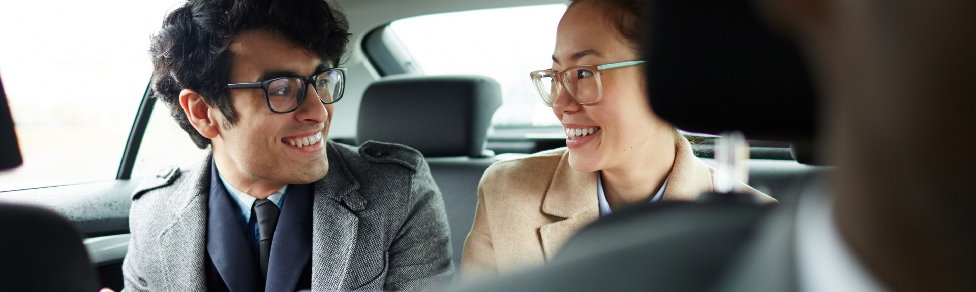 Two people smiling and talking in a car, dressed in business attire