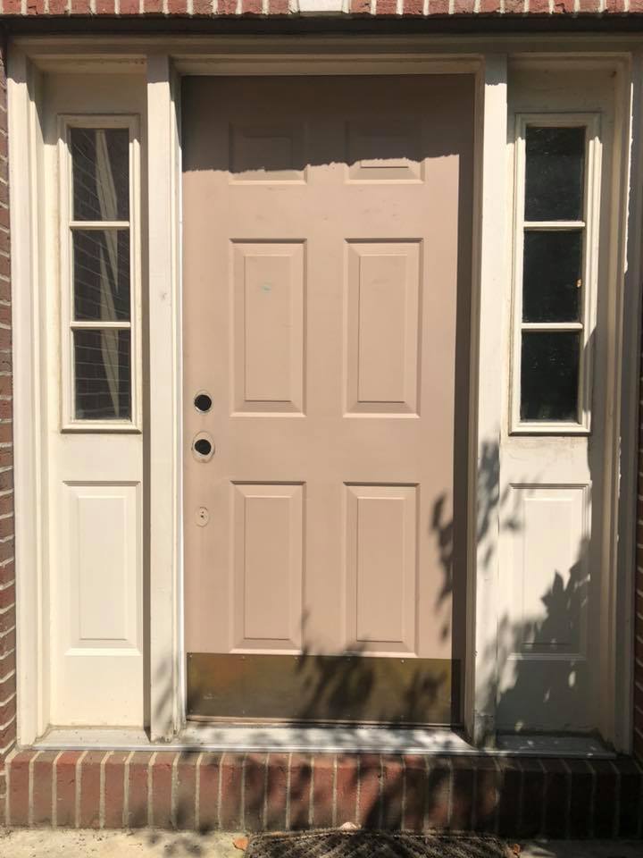 Tan front door with sidelights, set in brick and beige trim.