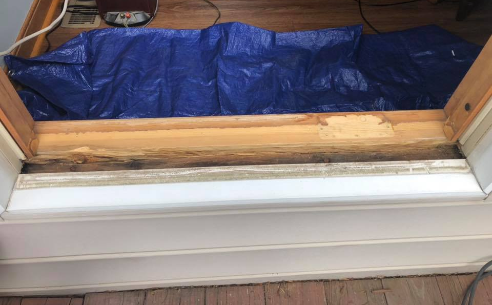 Damaged wooden door threshold with rotted wood and a blue tarp covering the floor.