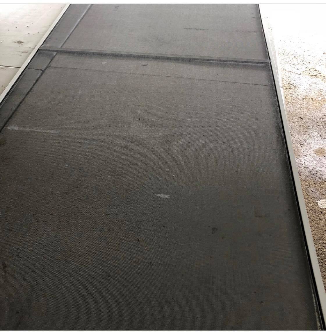 Dark gray rubber mat covering a floor area. Edges bordered by concrete and a beige surface.