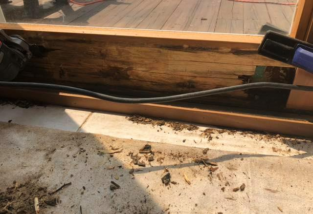Decayed wood window frame interior with debris, black cable, and ceramic tile.