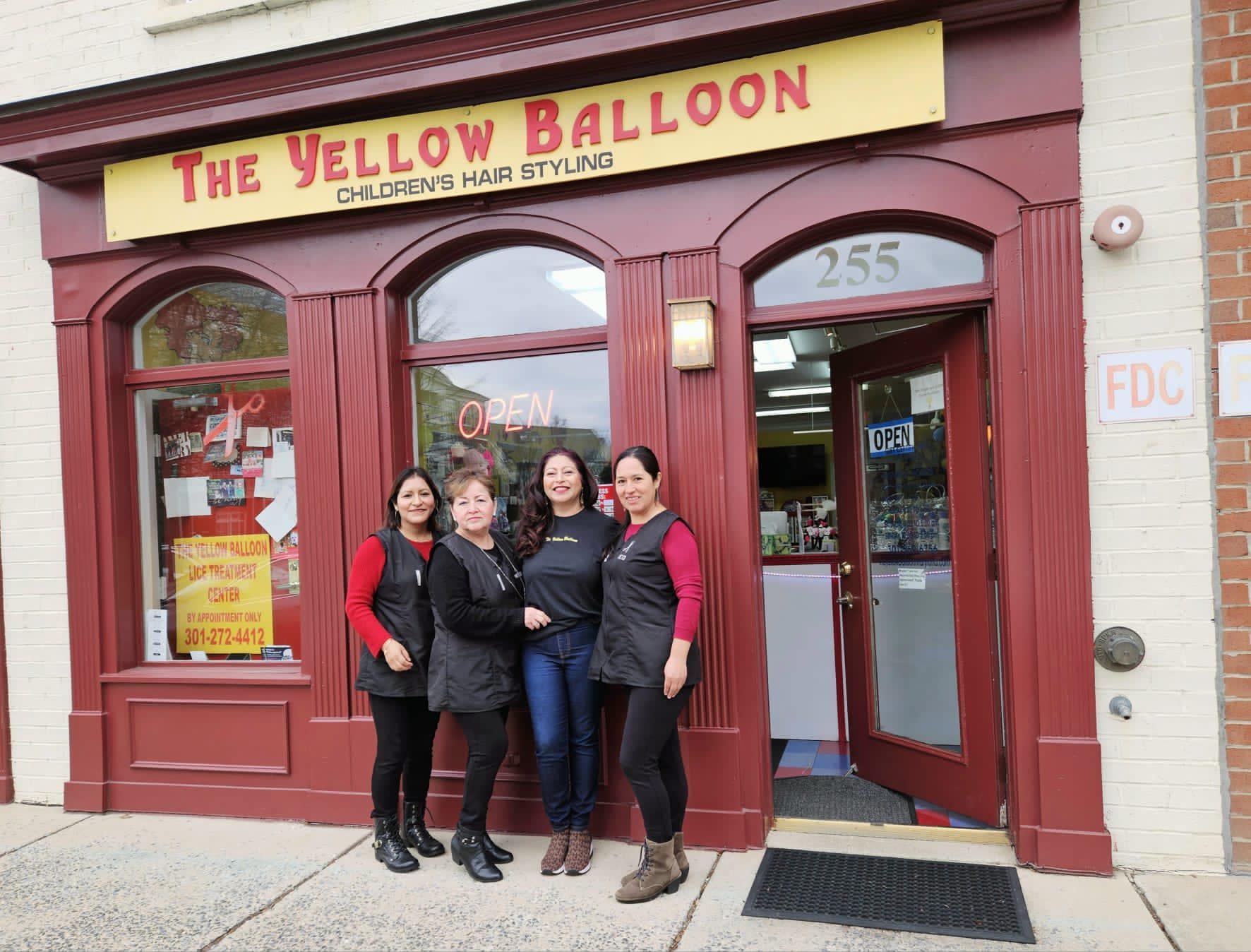 Four people posing outside The Yellow Balloon storefront with red facade and arched windows