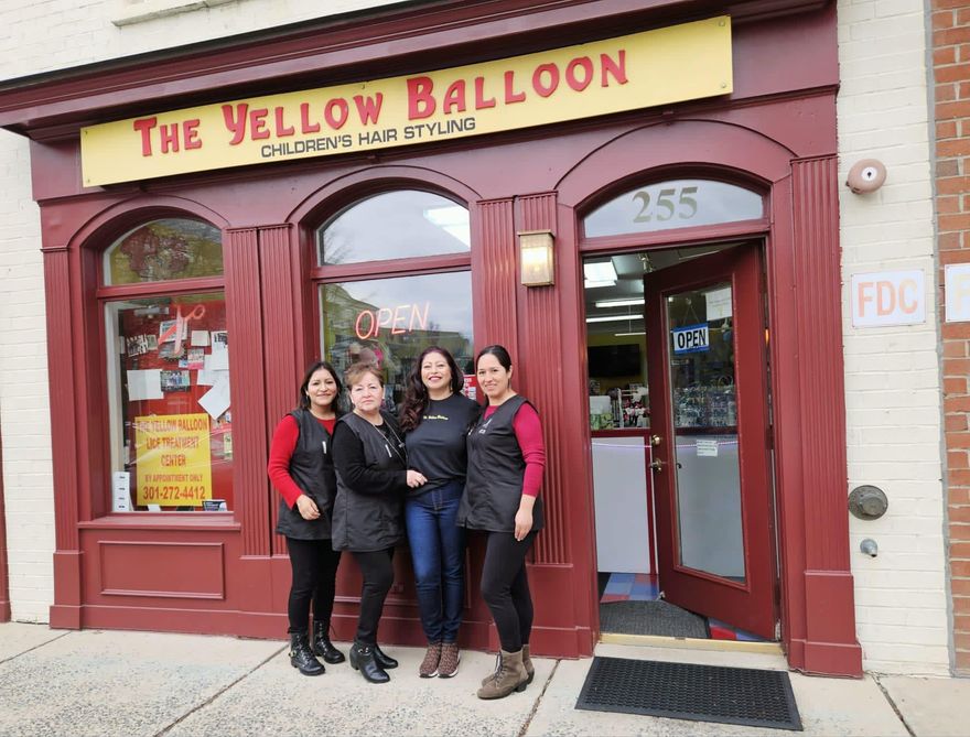 Four people posing outside The Yellow Balloon storefront, wearing black and red jackets.