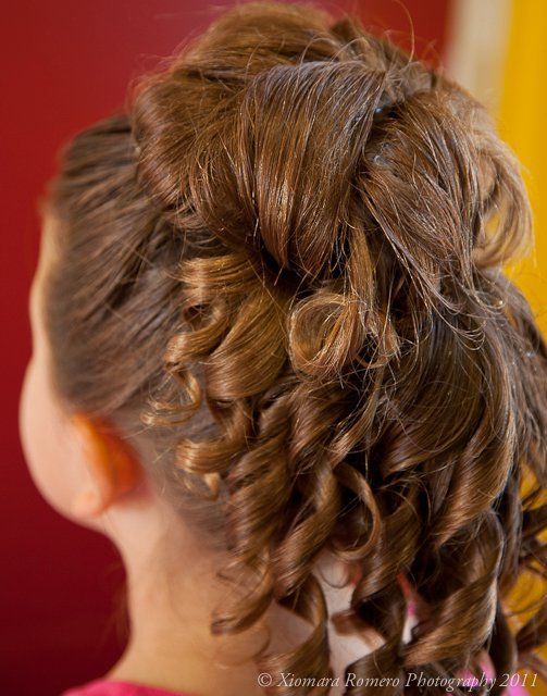 Close-up of an intricate braided updo hairstyle with curled strands, viewed from the back against a red background