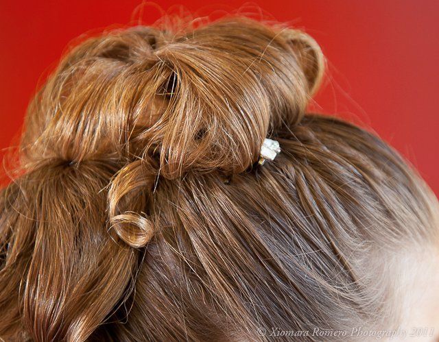 Close-up of a blonde updo hairstyle with a small white hair clip against a red background