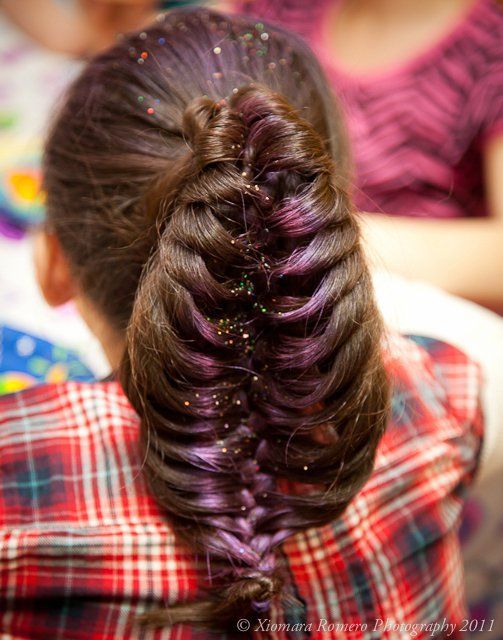 Braided dark hair with purple accents, viewed from behind, against a red plaid shirt.