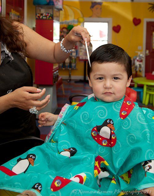 Child in a turquoise penguin cape gets a haircut in a colorful salon.