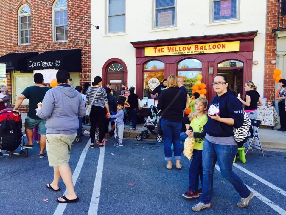Crowd gathered outside The Yellow Balloon storefront on a busy street, with people walking and chatting