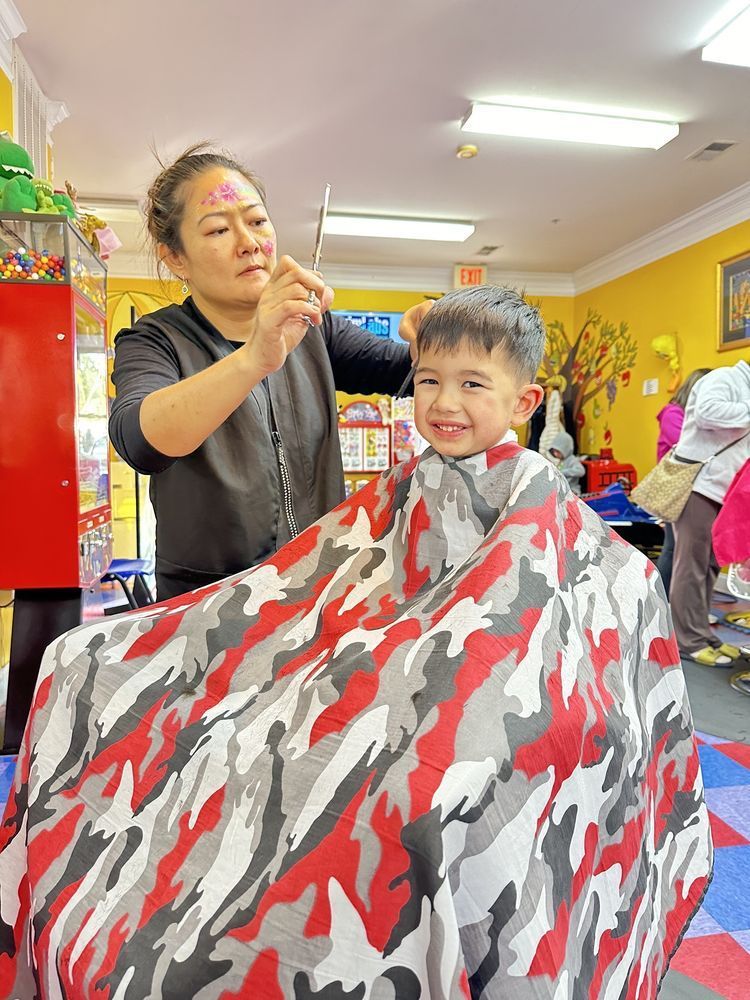 Young child with sparkly ponytail wearing a navy polka-dot shirt, seen from behind in a colorful indoor setting