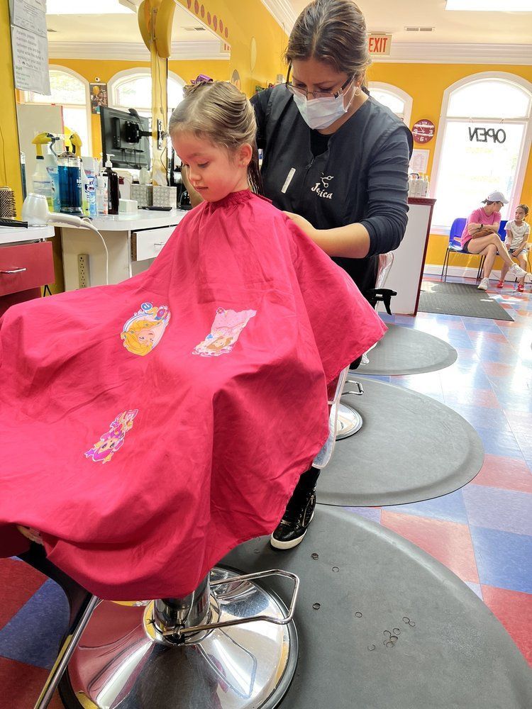 Woman cuts a child's hair in a brightly colored salon as a yellow balloon floats nearby.