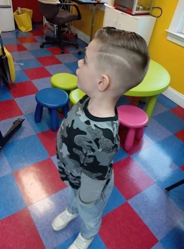 Woman cuts a child's hair in a brightly colored salon as a yellow balloon floats nearby.