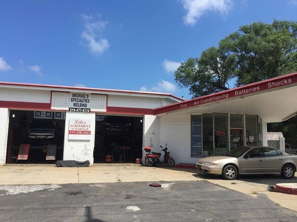 Small auto repair shop with open bays, parked car, and motorcycle under a blue sky.