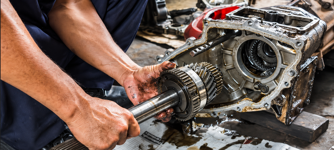 Mechanic repairing a car transmission with tools and grease-covered hands