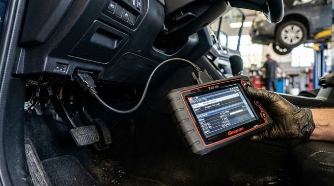 Mechanic using a handheld diagnostic scanner inside a car repair shop