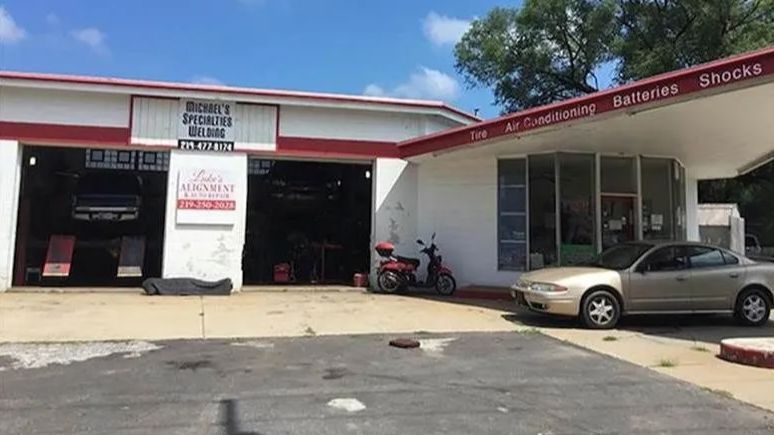 Auto repair shop with open bays, parked cars, and a motorcycle under a red-and-white awning