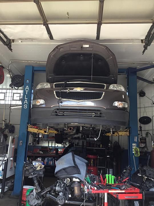 Car lifted on a blue auto lift in a garage, with a mechanic working underneath and tools nearby