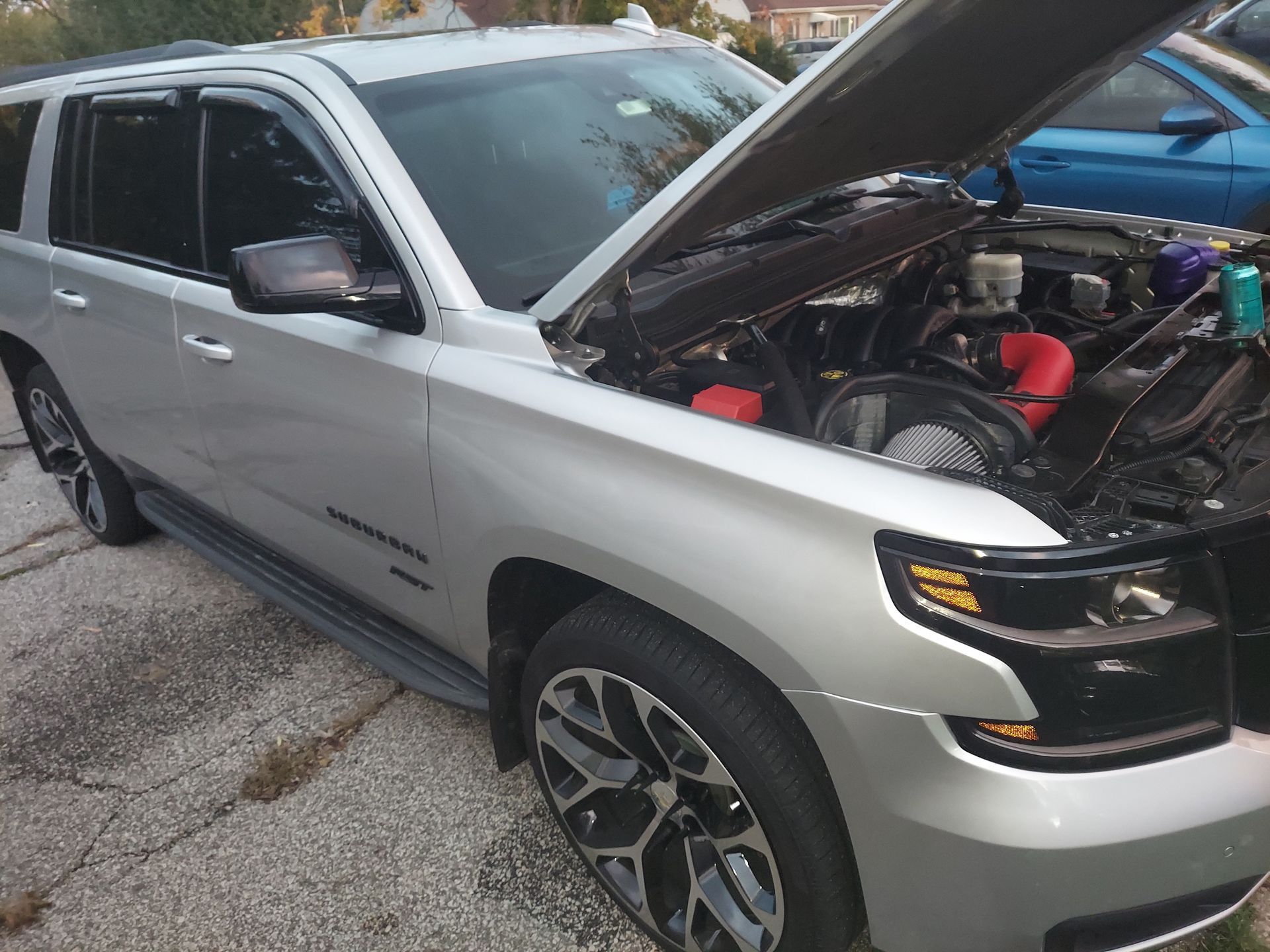 Silver SUV with hood open, revealing engine, parked outdoors near other vehicles.
