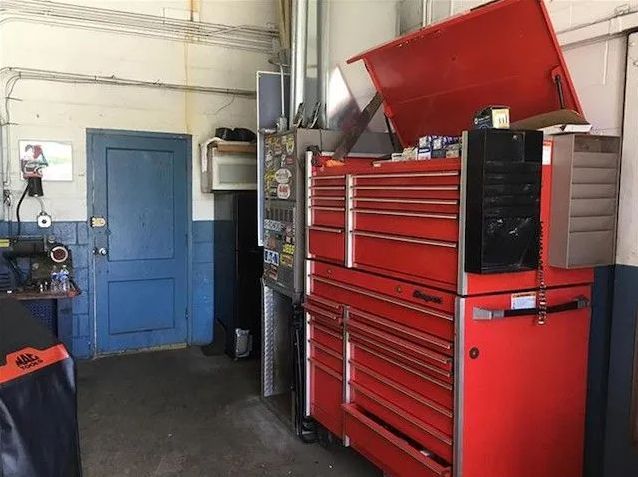 Red tool chest with open lid in a workshop beside a blue door and wall-mounted equipment.