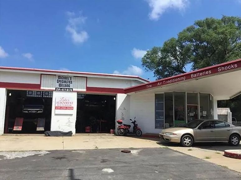 Auto repair garage with open bays, parked motorcycle and car, under a blue sky