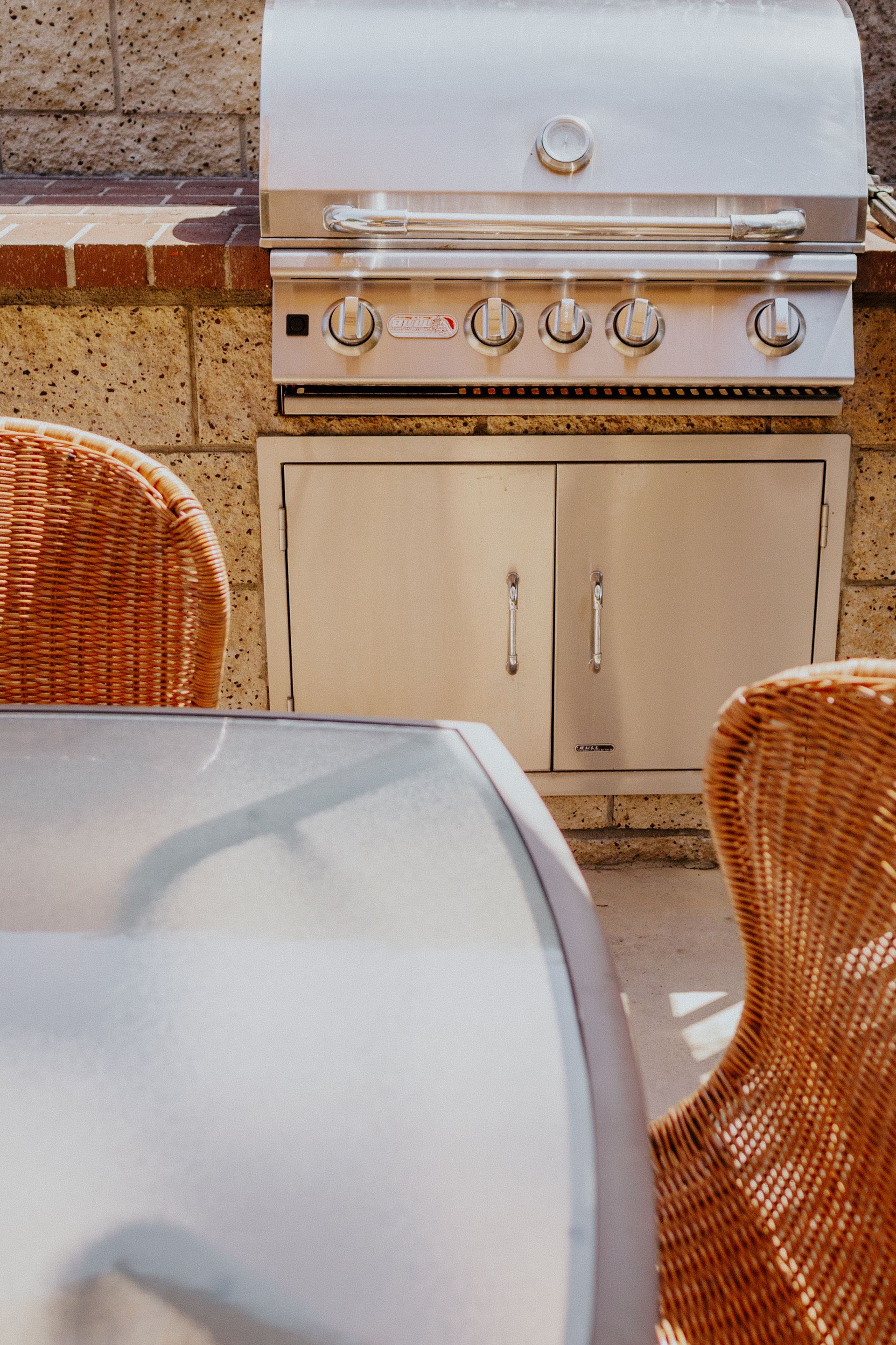 A grill is built into a brick wall next to a table and chairs.