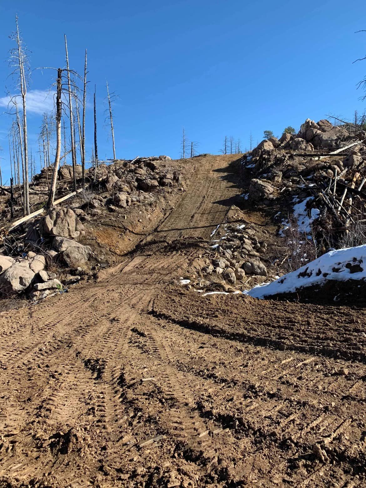 A dirt road going up a hill with snow on the ground.