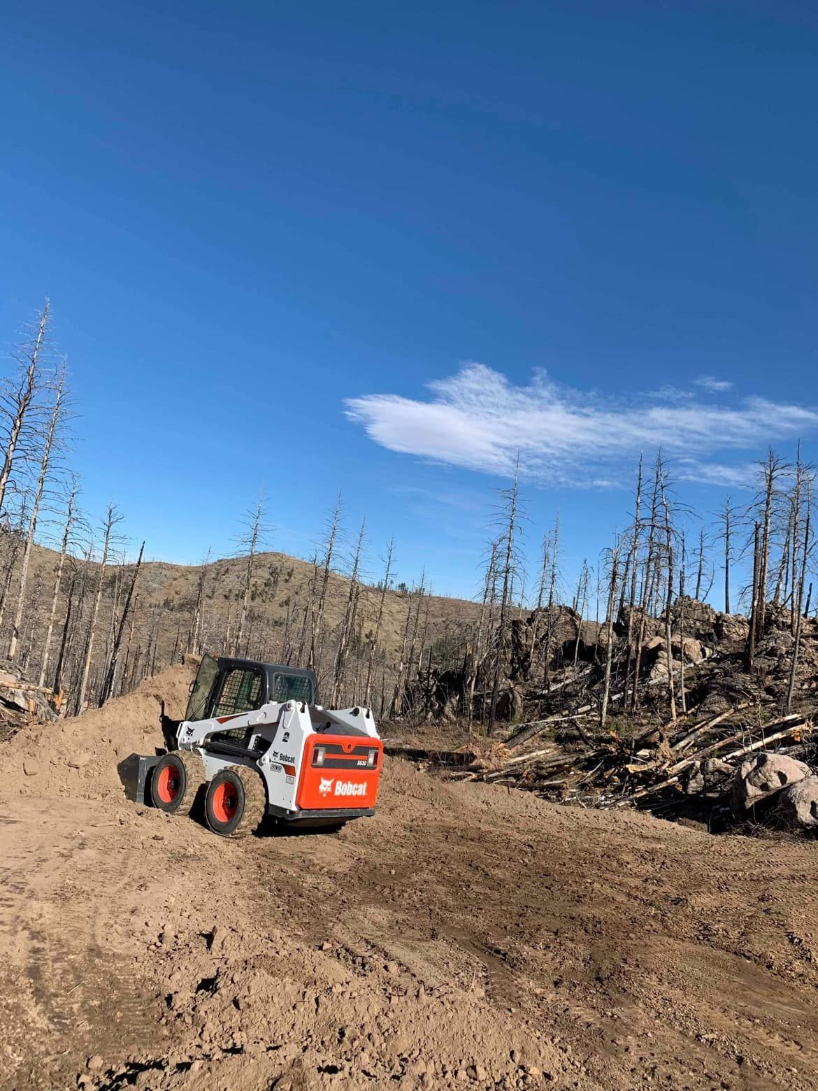 A bobcat skid steer is driving down a dirt road.