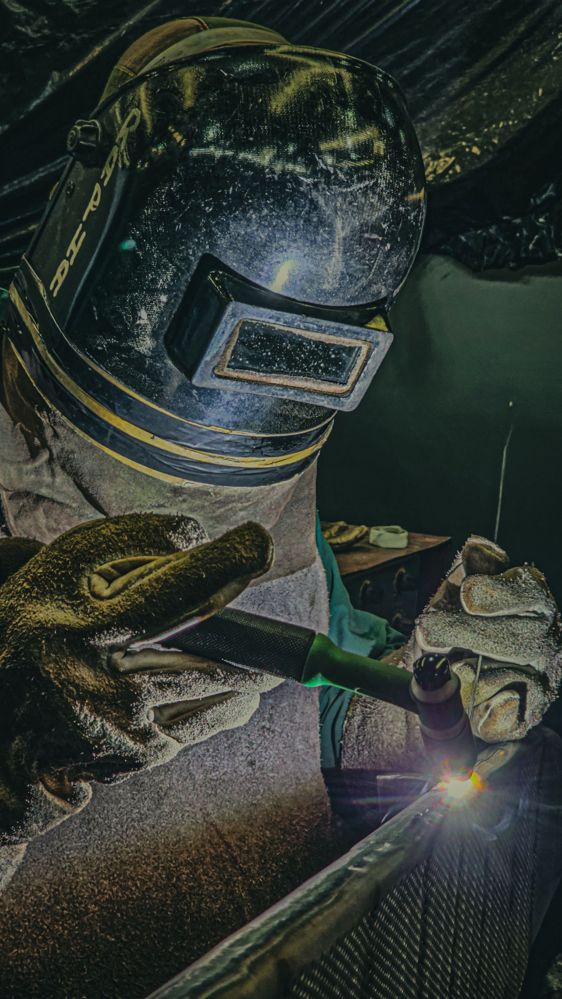 Welder in protective gear welding metal, bright sparks in a dark workshop