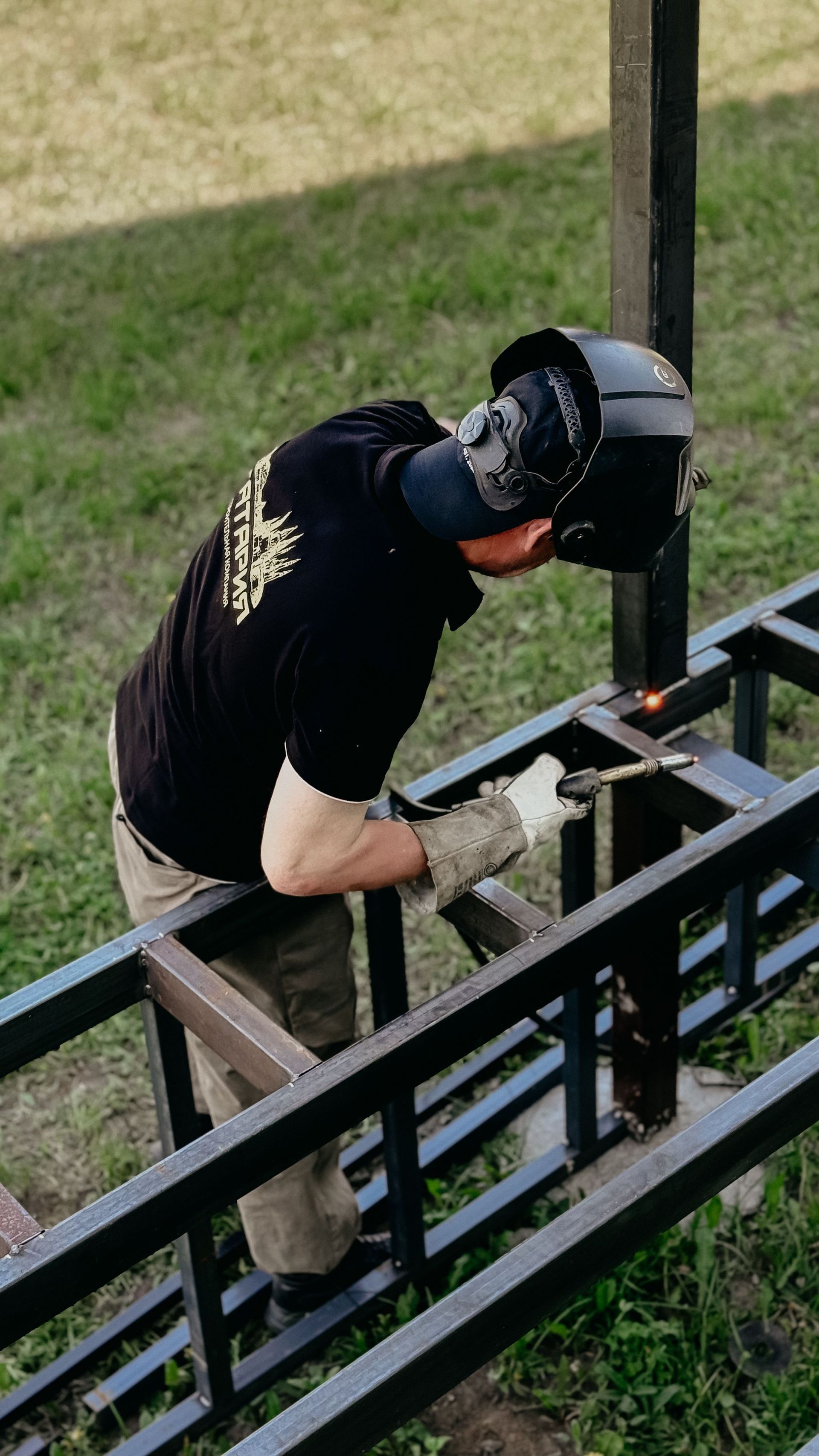 Worker welding a black metal railing outdoors on a grassy lawn