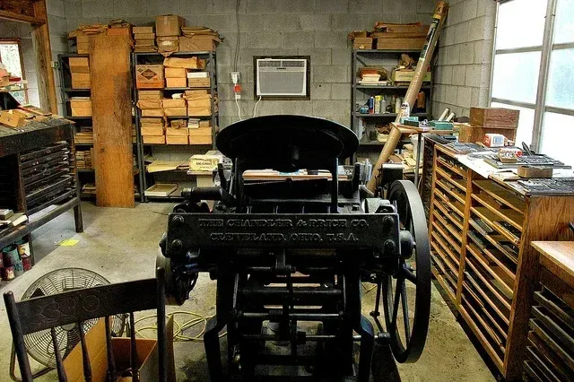 Old print shop with a printing press, shelves of paper, and wooden type cabinets