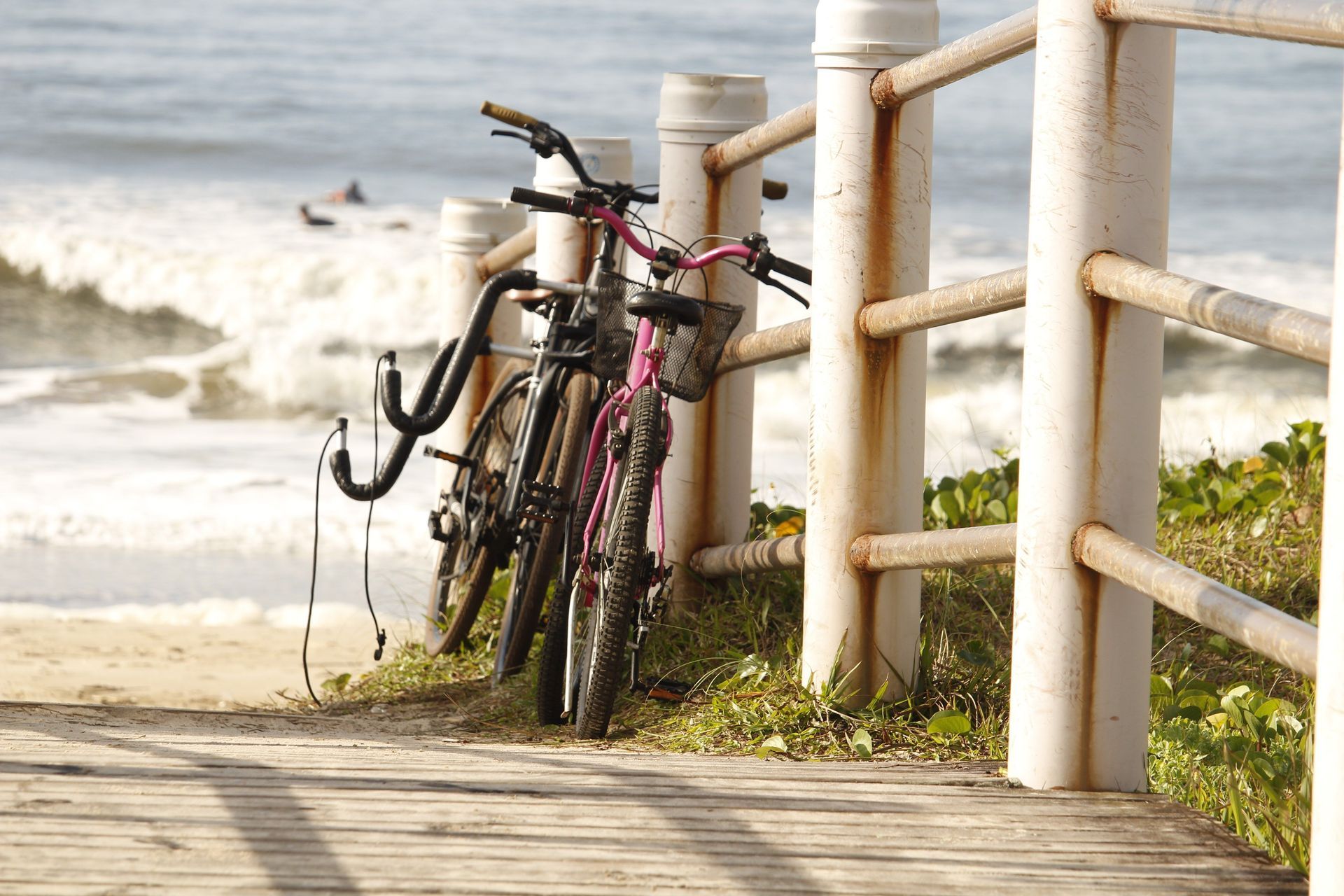 Two bicycles parked by a seaside railing on a sunny beach walkway