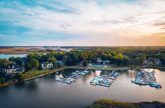 Aerial view of a marina with docked boats beside a tree-lined shoreline at sunset