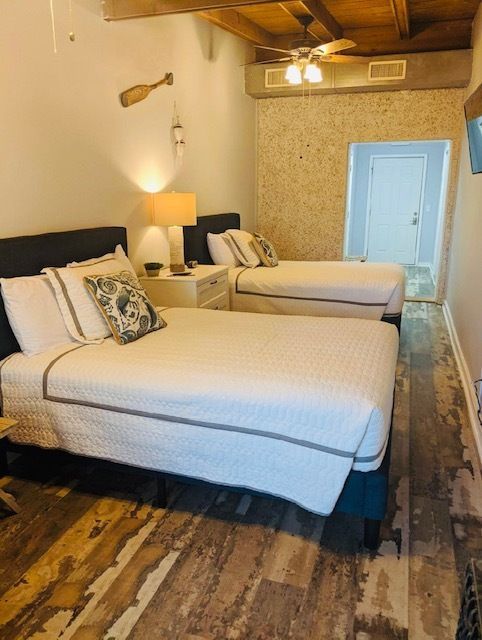 Hotel room with two twin beds, warm lamps, wood floor, and open doorway