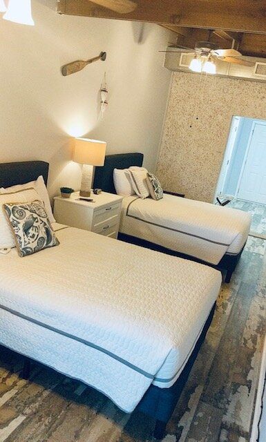 Small bedroom with two twin beds, white bedding, bedside lamp, and rustic ceiling beams.