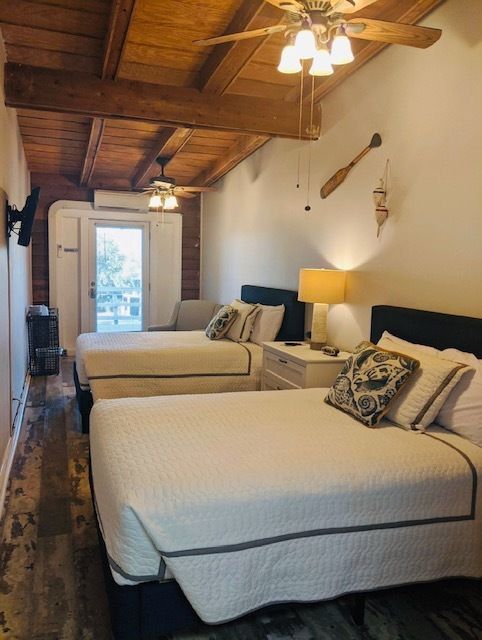 Rustic hotel room with two twin beds, wood ceiling, lamps, and a door to a balcony.