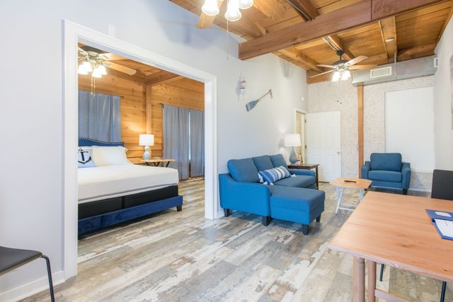Bright living room with blue chairs, wood ceiling, dining table, and an open bedroom doorway