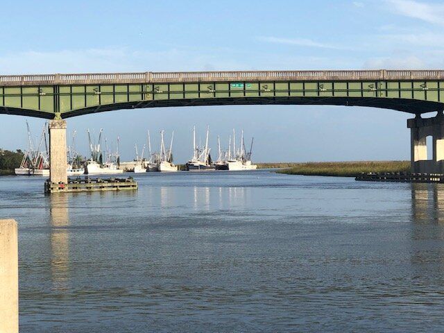 Green bridge over a calm river with sailboats and docks in the background