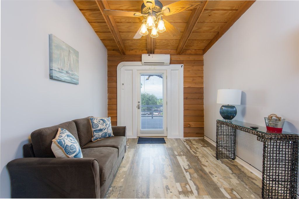 Bright living room with wood ceiling, gray sofa, patterned rug, and glass doors to a balcony.