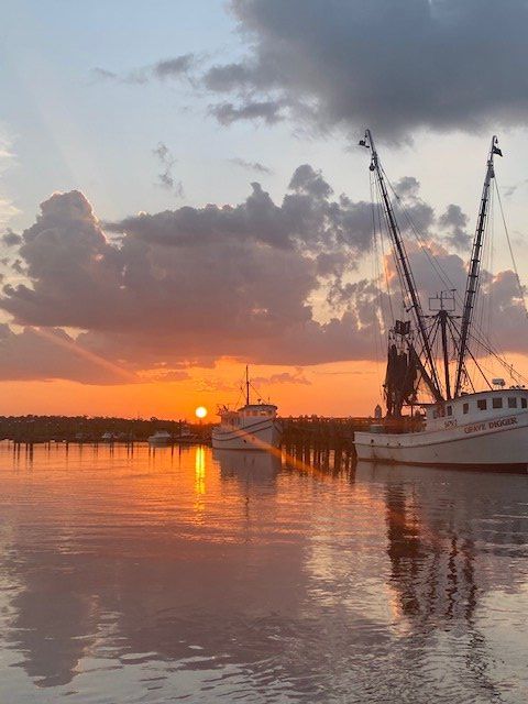 Sunset over a harbor with docked boats, cranes, and orange reflections on calm water
