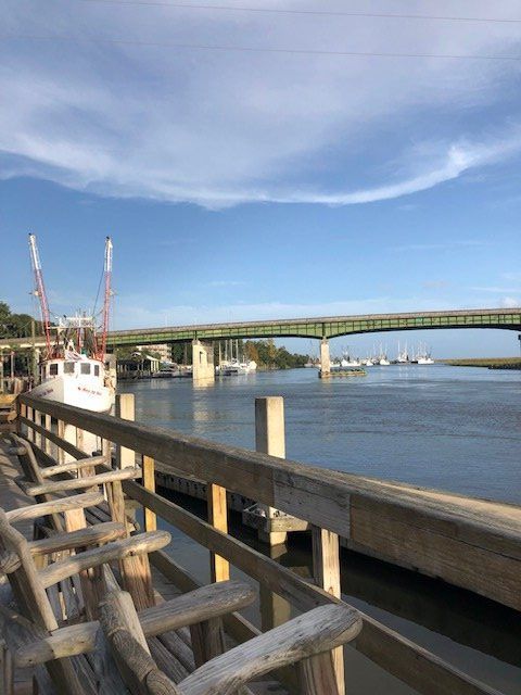 Wooden dock by a calm river with a green bridge and boats under a blue sky