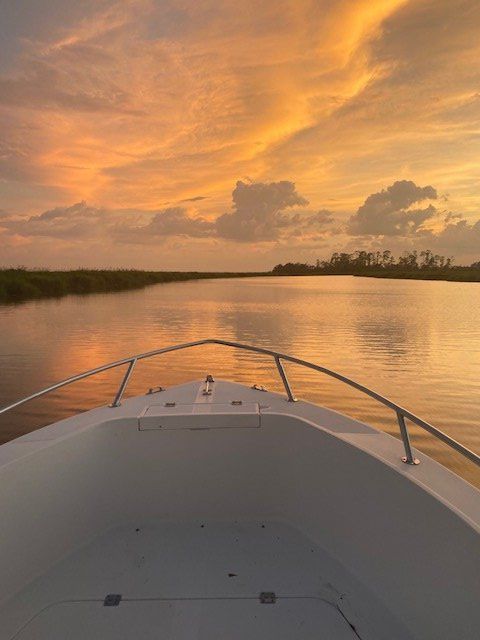 Boat bow at sunset on calm water with orange clouds and distant shoreline