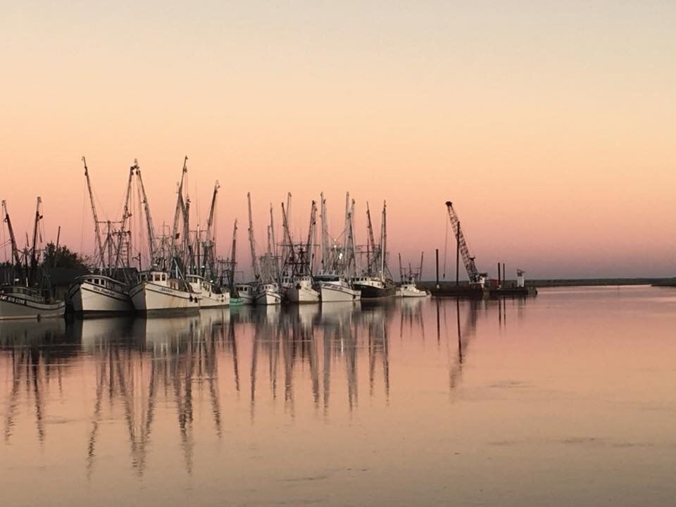 Fishing boats and tall masts reflected on calm water at sunset