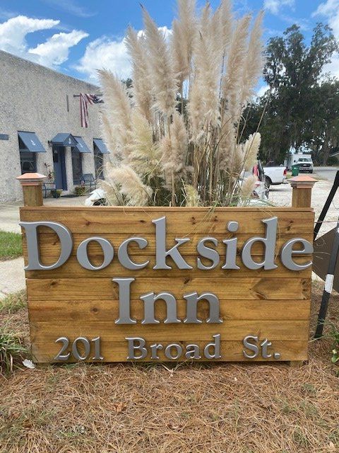 Wooden sign for Dockside Inn, 201 Broad St., with tall ornamental grass in front outdoors