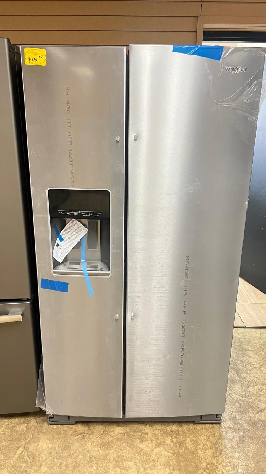 A stainless steel refrigerator with a water dispenser is sitting on a wooden floor.